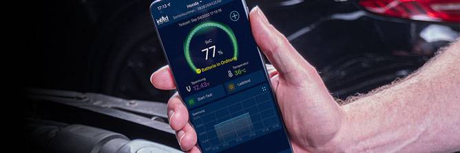 Teaser Battery-Guard - Ladezustand Das Bild zeigt ein Smartphone in der Hand vor einer Batterie. Darauf wird der Ladezustand in der Battery-Guard App angezeigt.